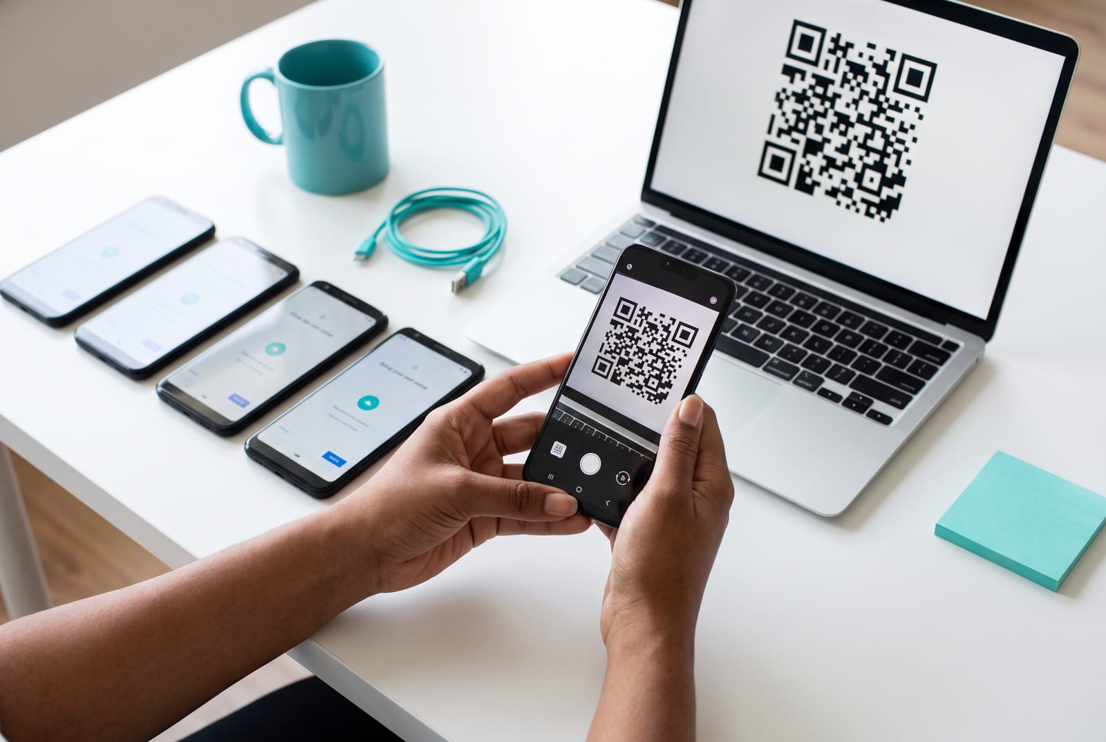 Hands scanning a QR code on a laptop with new Android phones on the table